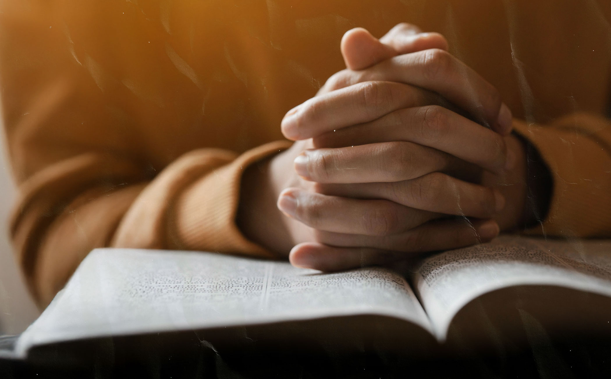 Man with folded hands on open Bible