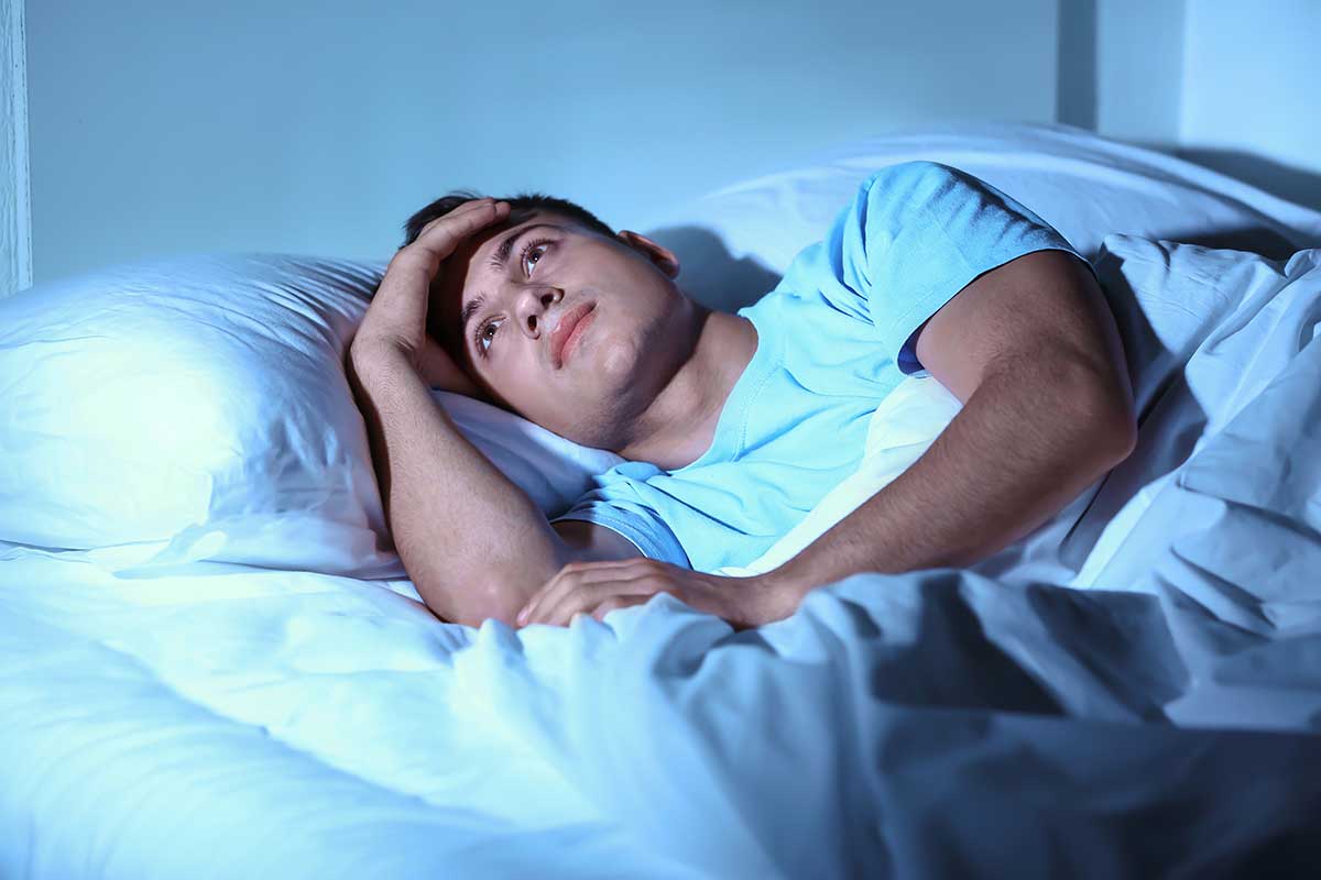 Young man suffering from insomnia while lying in bed at night